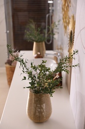 Vase with beautiful branches near vessel sink in bathroom. Interior design