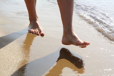 Woman walking on sandy seashore, closeup of legs