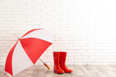 Beautiful colorful umbrella and rubber boots near white brick wall. Space for text