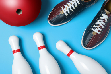 Bowling ball, shoes and pins on light blue background, flat lay