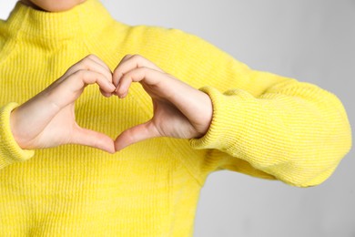 Photo of Woman making heart with her hands on light grey background, closeup