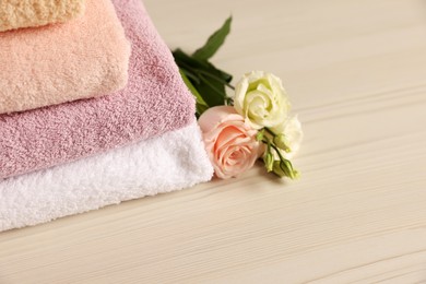 Soft folded towels, rose and eustoma flowers on light wooden table, closeup