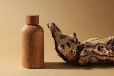Photo of Wooden bottle of cosmetic product and tree bark on dark beige background