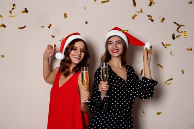 Happy women in Santa hats with champagne and confetti on beige background. Christmas party