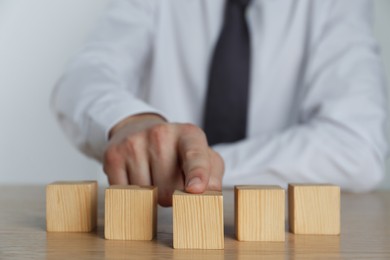 Businessman arranging blank cubes on wooden table, closeup. Space for text