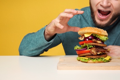 Photo of Young man with tasty huge burger at table