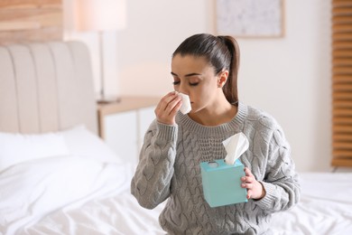 Ill woman with box of paper tissues on bed at home