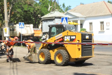 MYKOLAIV, UKRAINE - AUGUST 04, 2021: Workers with road repair machinery laying new asphalt, focus on construction tape