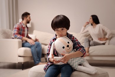 Sad little boy with toy and his arguing parents on sofa in living room