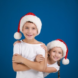 Happy little children in Santa hats on blue background. Christmas celebration