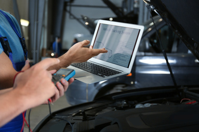 Mechanics with laptop doing car diagnostic at automobile repair shop, closeup