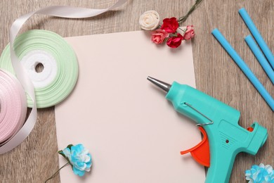 Photo of Hot glue gun and handicraft materials on wooden table, flat lay. Space for text