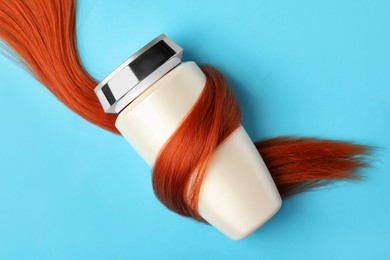 Bottle wrapped in lock of hair on light blue background, top view. Natural cosmetic product