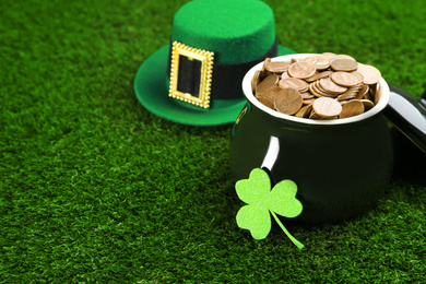 Pot of gold coins, hat and clover on green grass, space for text. St. Patrick's Day celebration