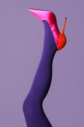 Woman wearing bright tights and high heel shoe on violet background, closeup