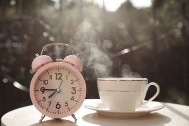 Photo of Pink alarm clock and cup with hot drink on white table in morning