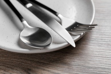 Photo of Plate with shiny silver cutlery on wooden table, closeup