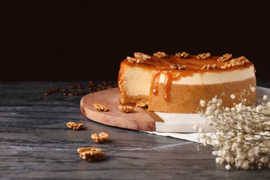 Photo of Delicious cheesecake with caramel and walnuts on black marble table, space for text