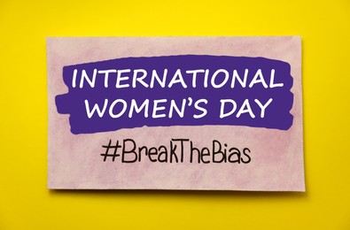 Card with text International Women's Day and hashtag BreakTheBias on yellow background, top view
