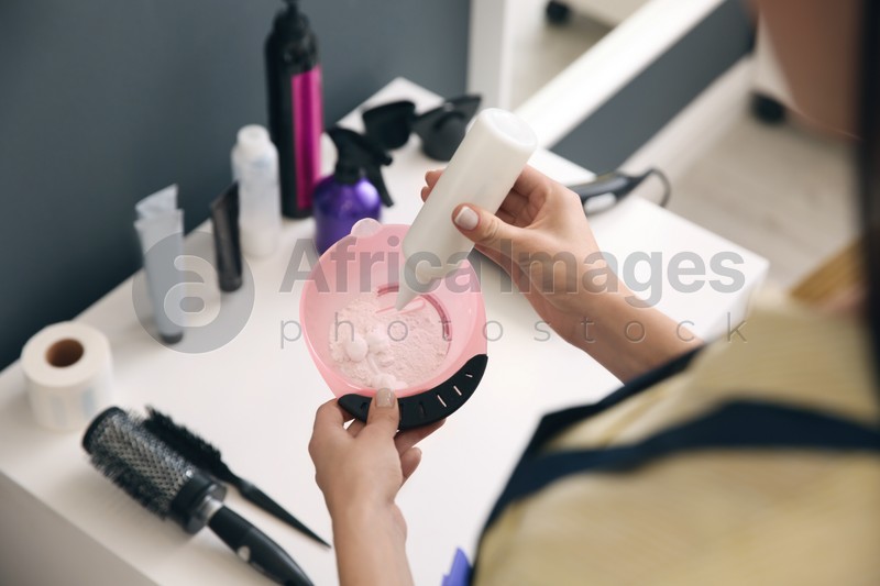 Professional hairdresser preparing dye for hair coloring in beauty salon, closeup