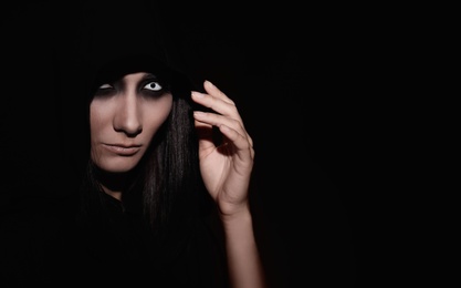 Mysterious witch with spooky eyes on black background, space for text