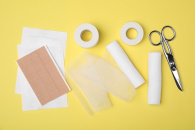 White bandage rolls and medical supplies on yellow background, flat lay