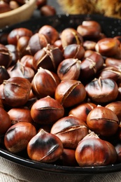 Delicious roasted edible chestnuts in frying pan on table, closeup