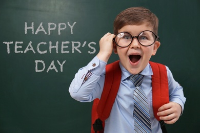 Emotional little child wearing glasses near chalkboard with text Happy Teacher's Day