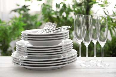 Set of clean dishware, cutlery and champagne glasses on white table against blurred background