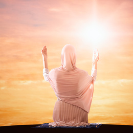 Muslim woman in traditional clothes praying at sunrise, back view. Holy month of Ramadan