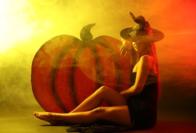 Young woman wearing witch costume near decorative pumpkin in smoke cloud. Halloween party