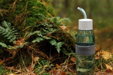 Photo of Glass bottle of fresh water on ground in forest, space for text