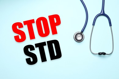 Text STOP STD and stethoscope on light blue background, top view