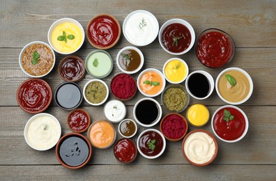 Many different sauces and herbs on wooden table, flat lay