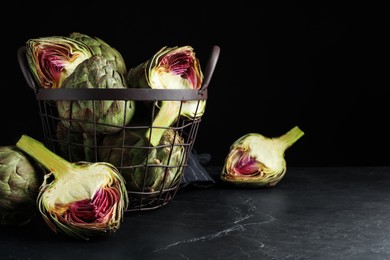 Cut and whole fresh raw artichokes on black table, space for text
