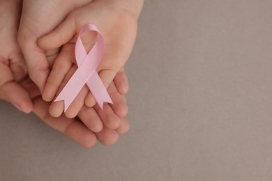 Family holding pink ribbon on grey background, top view with space for text. Breast cancer awareness