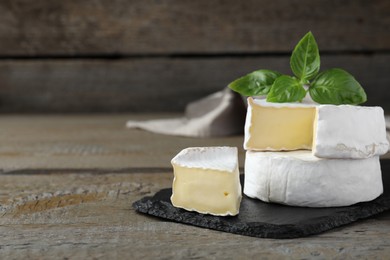 Tasty cut and whole brie cheeses with basil on wooden table, space for text