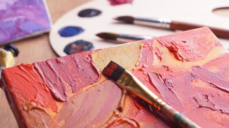 Photo of Artist's canvas with mixed paints and brush on wooden table, closeup