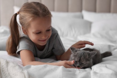 Photo of Cute little girl with kitten on bed. Childhood pet