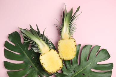 Photo of Halves of pineapple and palm leaves on pink background, flat lay