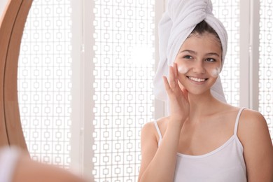 Beautiful teenage girl applying cleansing foam onto face near mirror at home, space for text. Skin care cosmetic