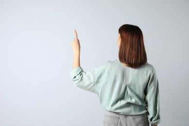 Young girl pointing on white background, back view. Space for text