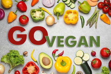 Phrase Go Vegan and fresh vegetables on light grey background, flat lay