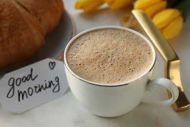 Cup of coffee, croissant and card with phrase GOOD MORNING on white tray, closeup