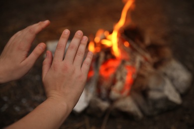 Woman warming hands near burning firewood outdoors, closeup