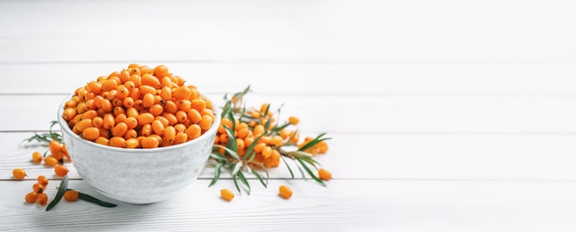 Fresh ripe sea buckthorn in bowl on white wooden table, space for text. Banner design