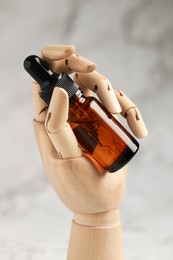 Photo of Bottle of organic cosmetic product in wooden mannequin hand on light marbled background, closeup