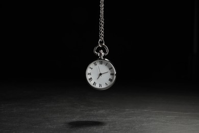Beautiful vintage pocket watch with silver chain on black background above dark table. Hypnosis session