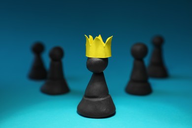 Black plasticine chess pieces and one with paper crown on light blue background