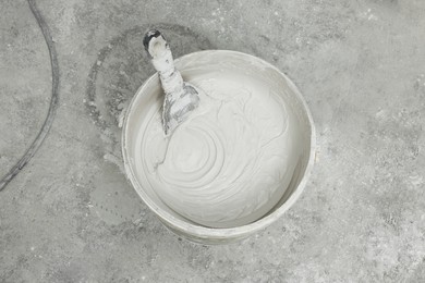 Bucket with plaster and putty knife on concrete floor, top view